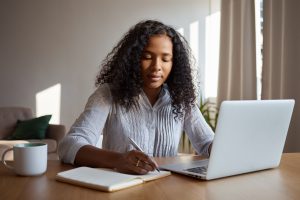 moça negra jovem escreve em seu laptop textos para blog corporativo