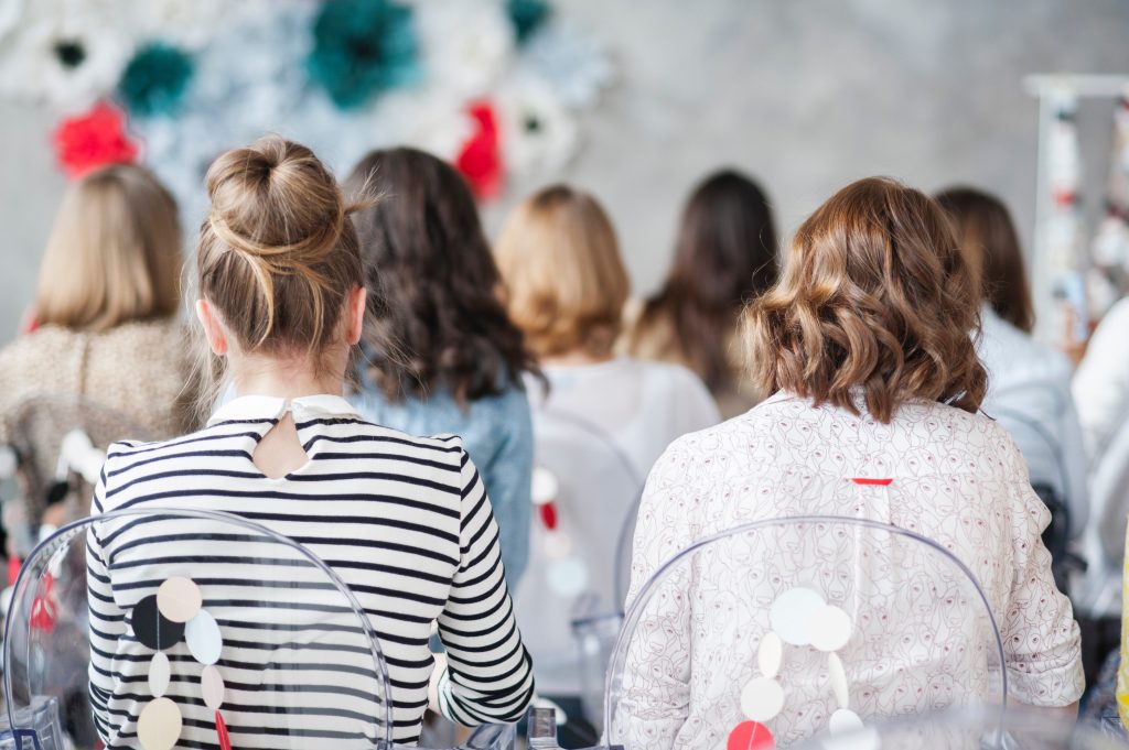 Mulheres sentadas de costas ouvem o roteiro do evento (Imagem: Pexels)