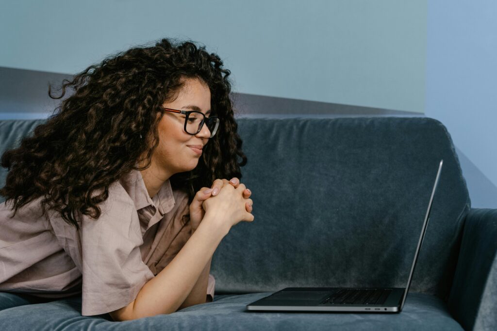 Imagem de uma mulher deitada em um sofá, olhando para seu notebook. Foto: Freepik