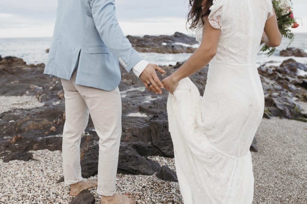 Foto de um casal de noivos caminhando na praia. Imagem: Magnific.